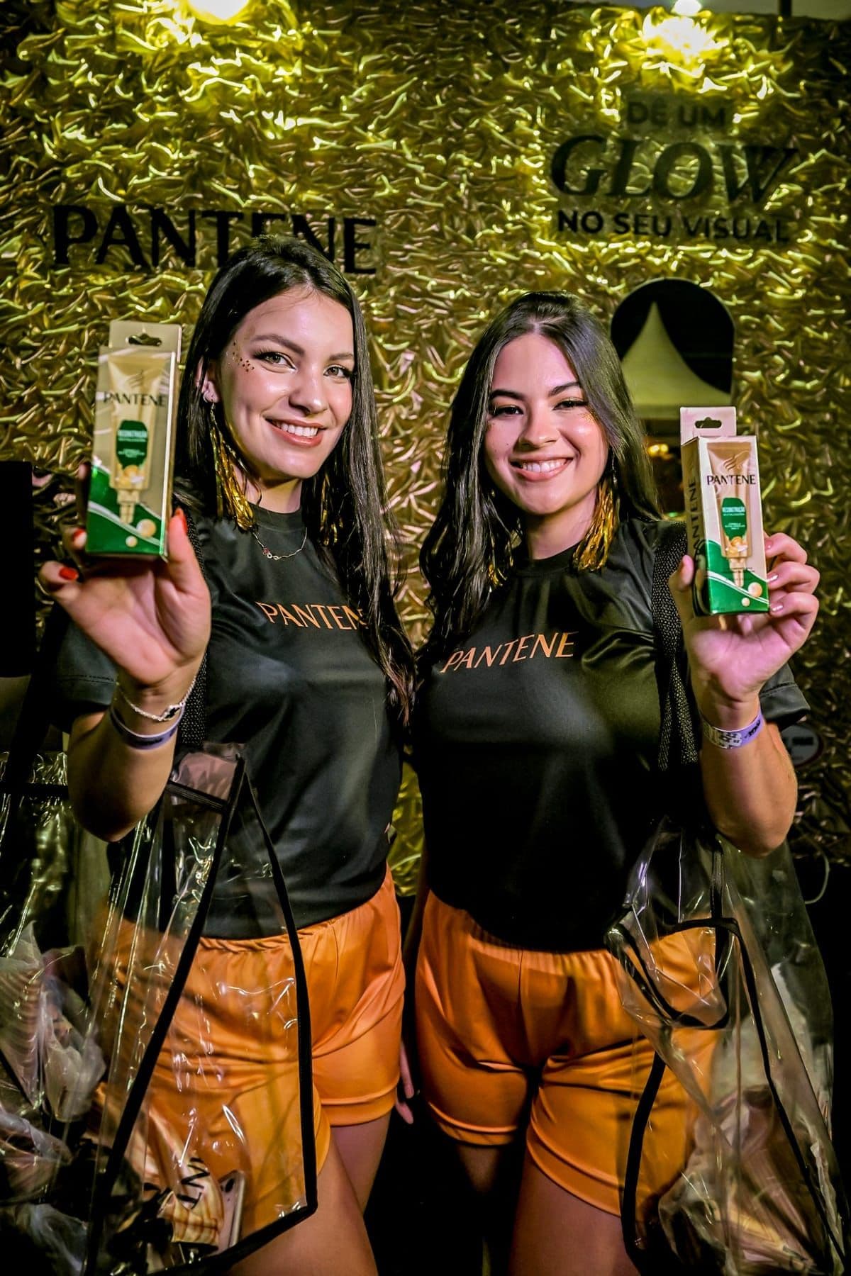 Dupla de promotoras Pantene entregando amostras em frente ao painel dourado